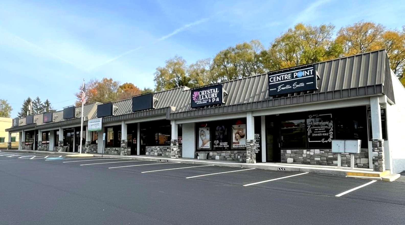 Exterior view of a strip mall with several businesses, a parking lot, and a blue sky.
