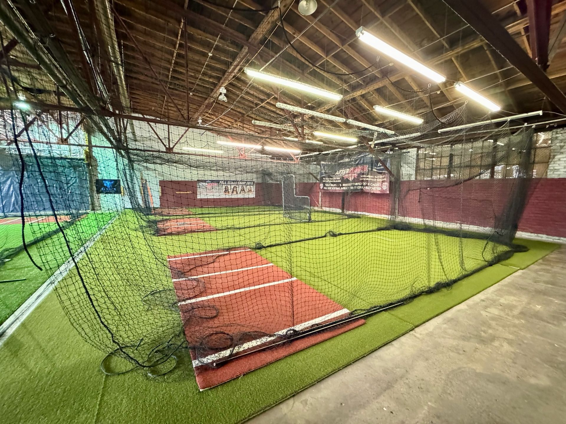Indoor baseball training facility with netting, artificial turf, and batting cages.