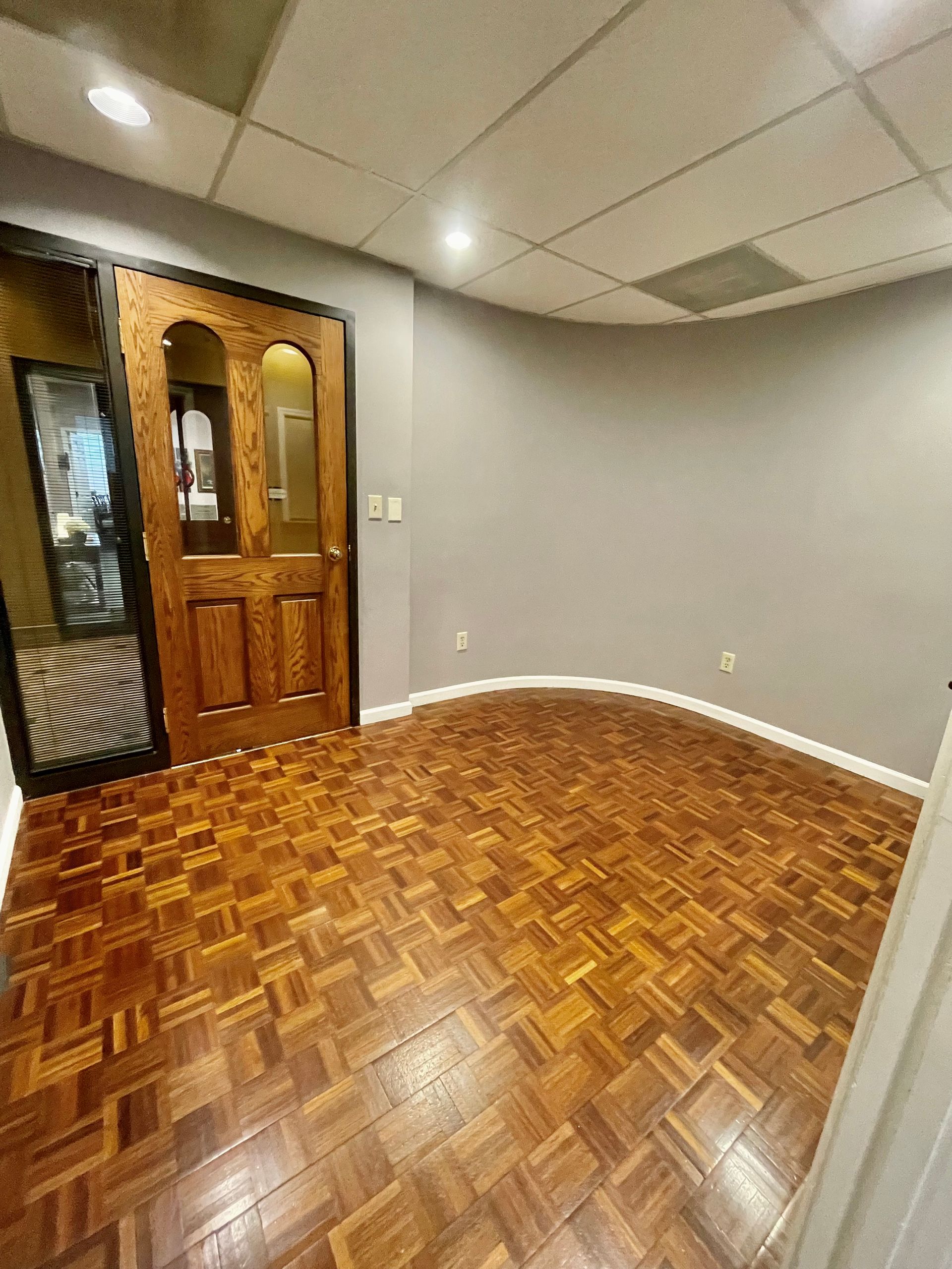 Wooden floor, gray walls, brown door, small room with overhead lighting.