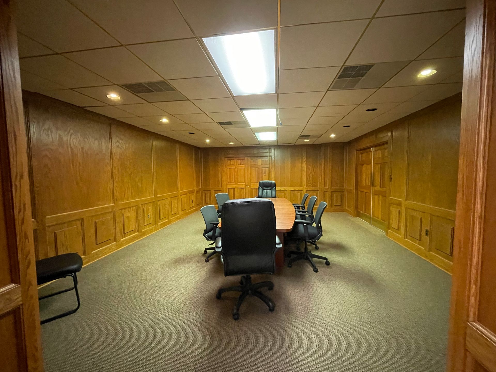 Conference room with wood paneling, oval table, and chairs; open doorway.