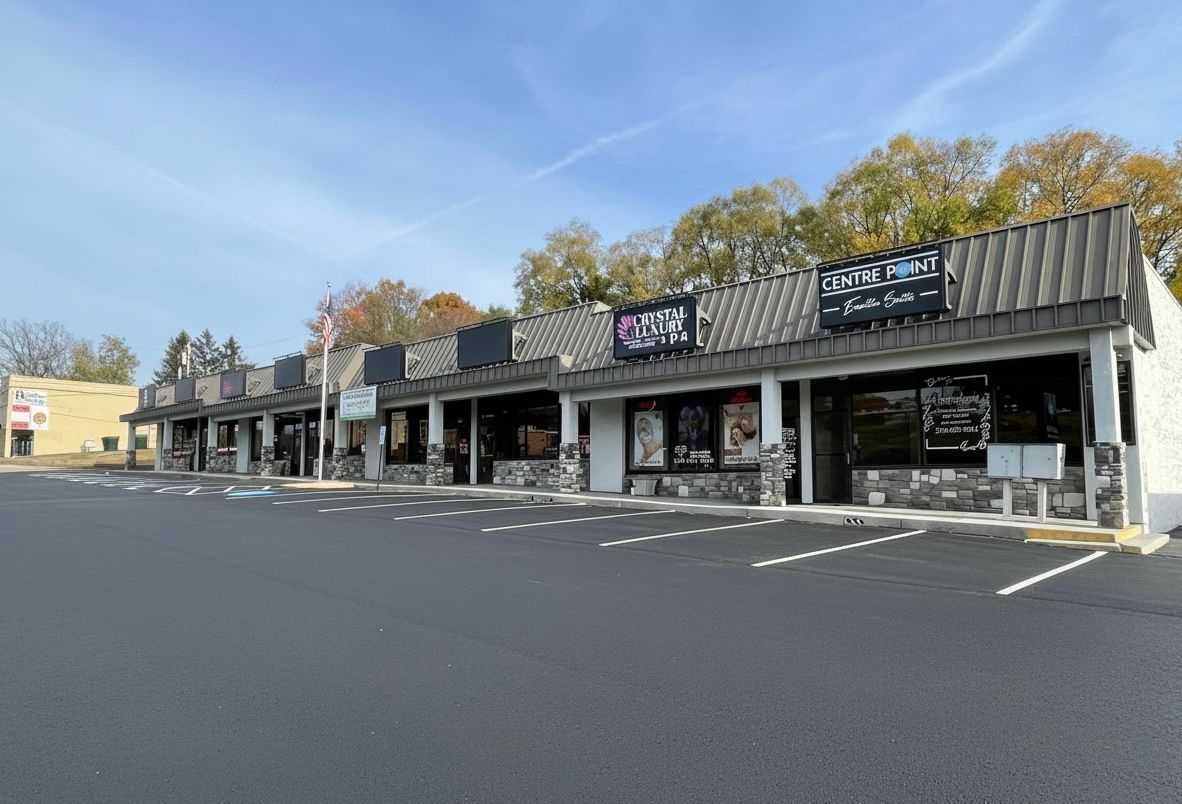 Strip mall storefronts under a partly cloudy sky with some tree foliage visible.