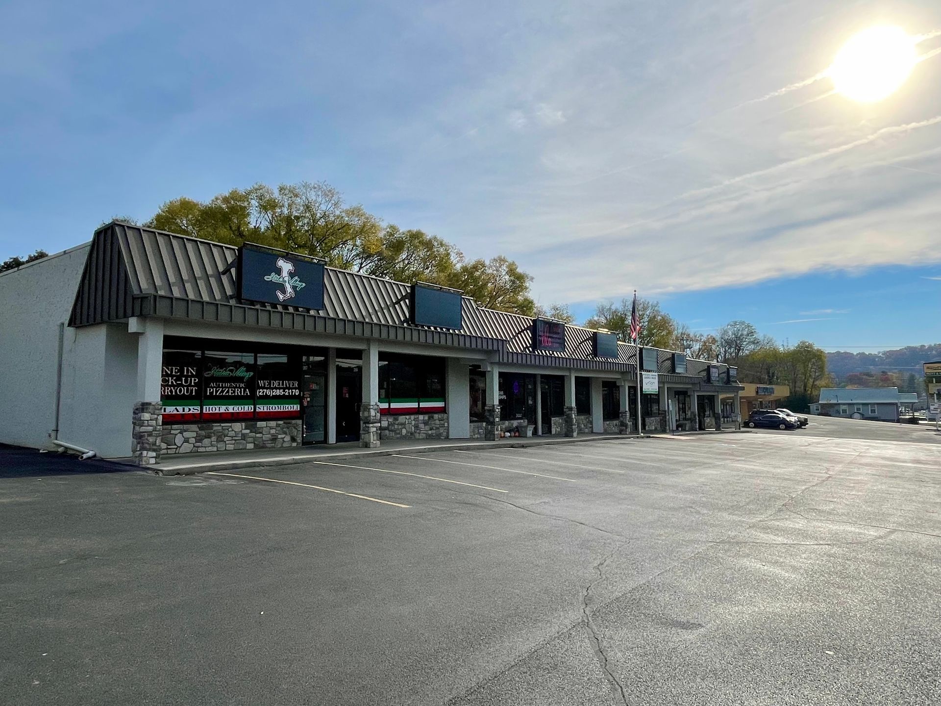 Exterior of a strip mall with a dark roof and large windows on a sunny day.