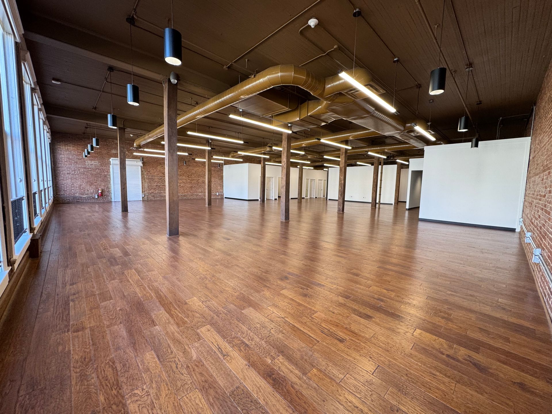 Empty event space with wood floors, exposed brick, and ceiling beams.