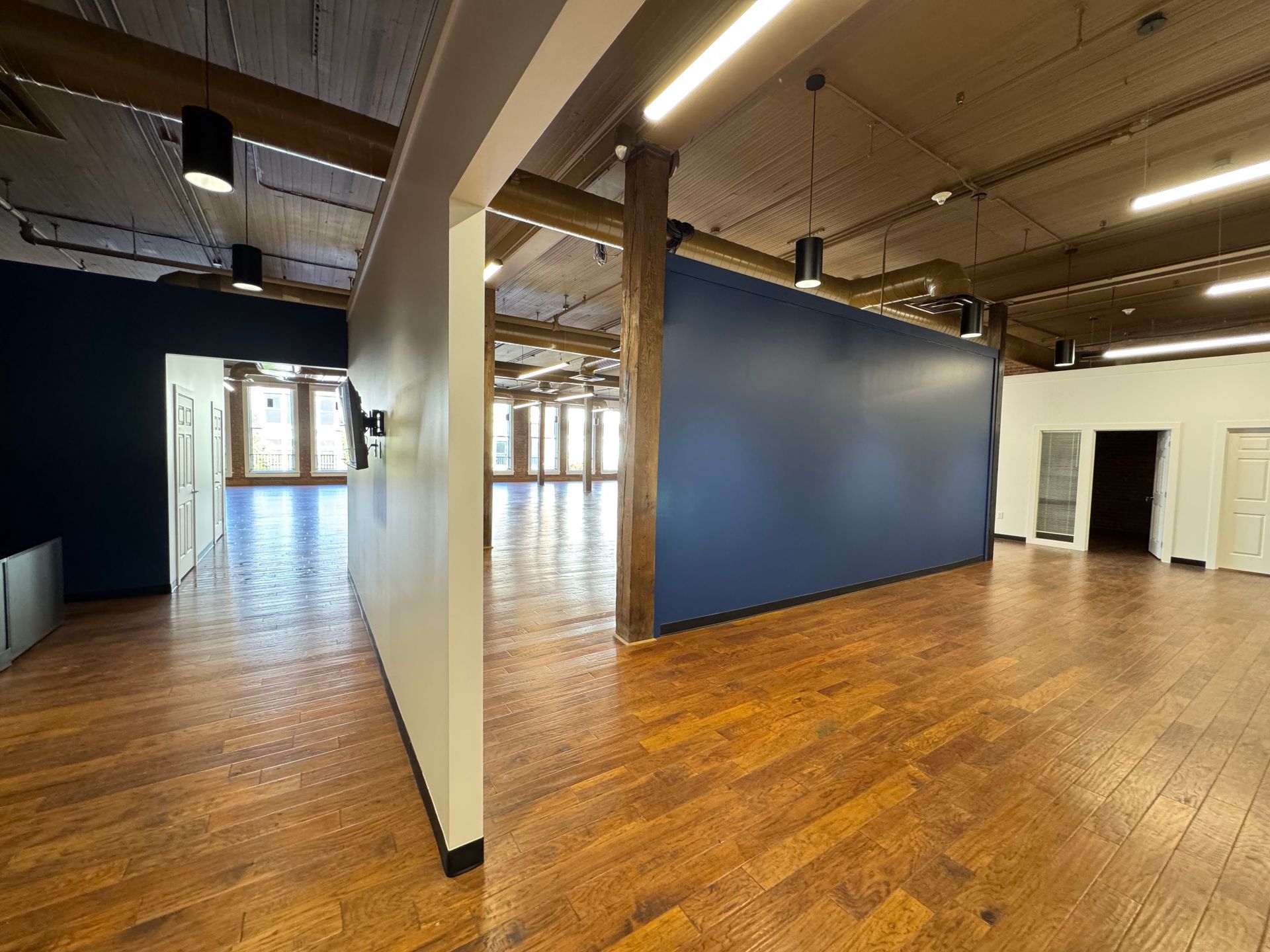 Empty room with hardwood floors, navy and white walls, and exposed beams with new 8 foot tall LED Display - After picture