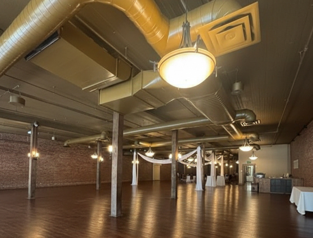 Large, open event space with wood floors, brick walls, and exposed pipes and lighting - Before Picture