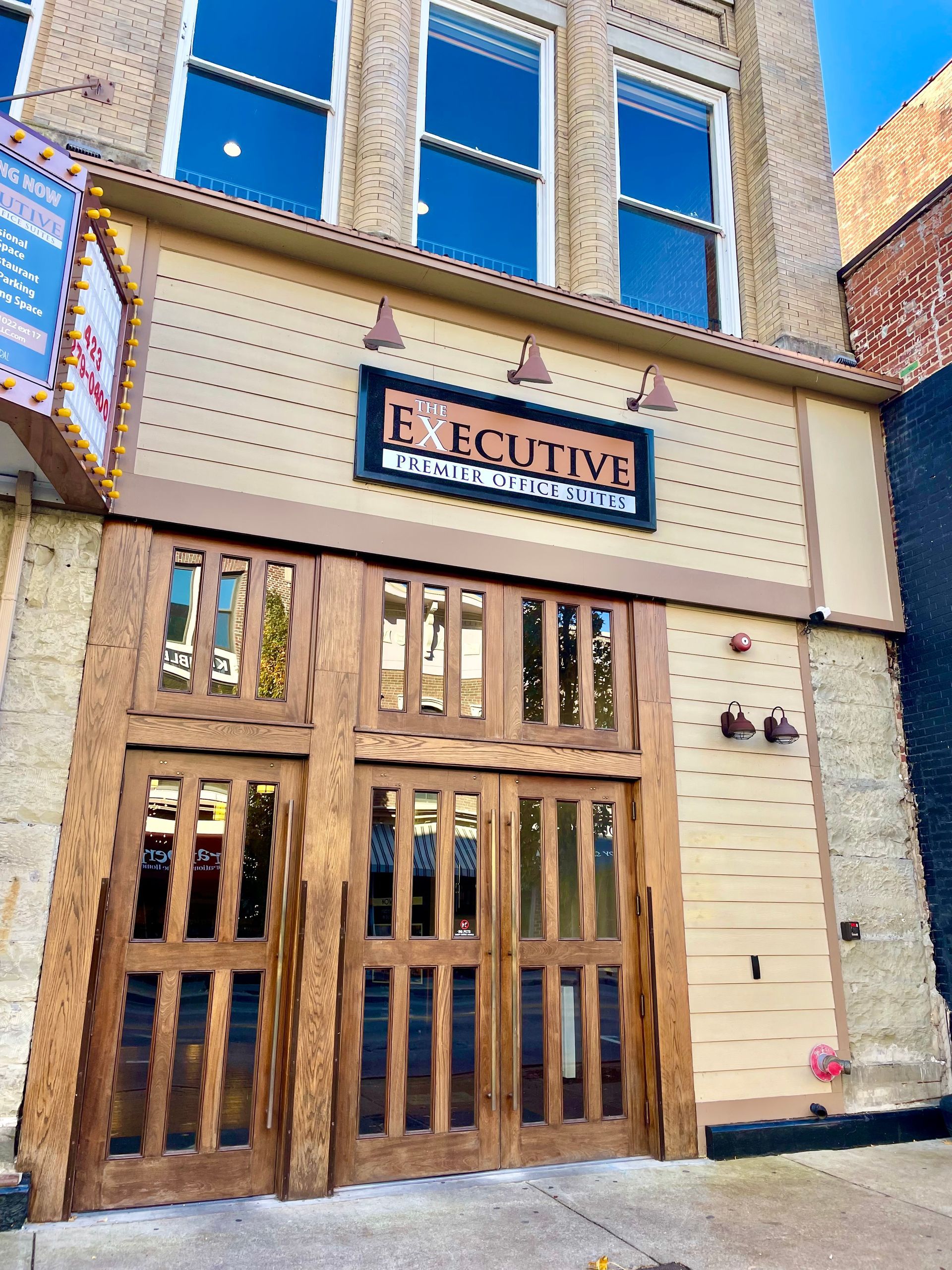 Executive Bar entrance with wooden doors and signage, tan facade, brick building background.