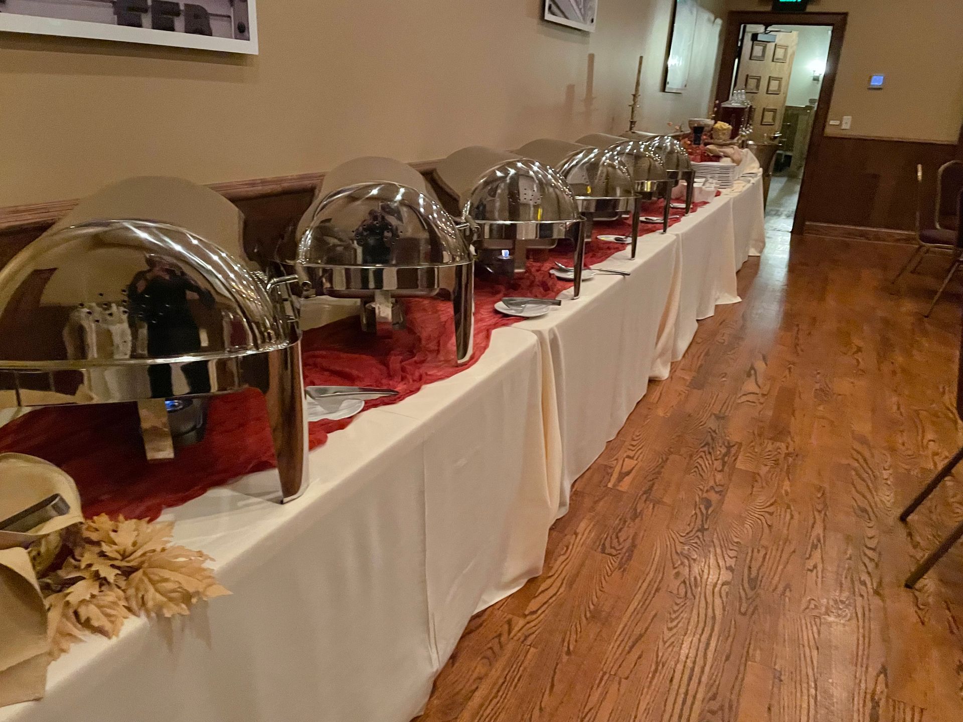 A buffet table with several stainless steel chafing dishes covered with lids on a long table with a cream-colored cloth.