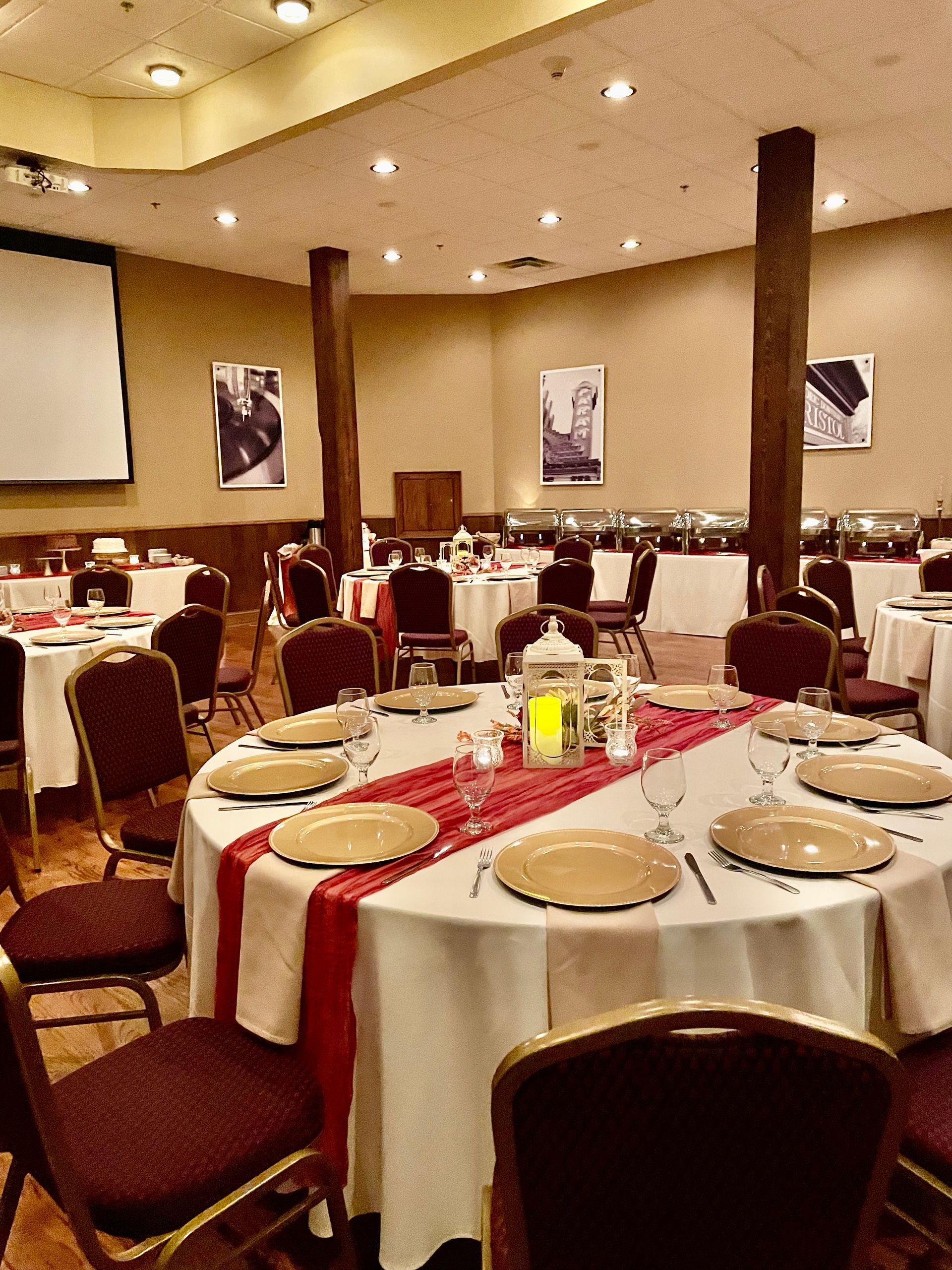 Formal dining room set for a banquet. Round tables with white cloths and red runners; chairs and plates set.
