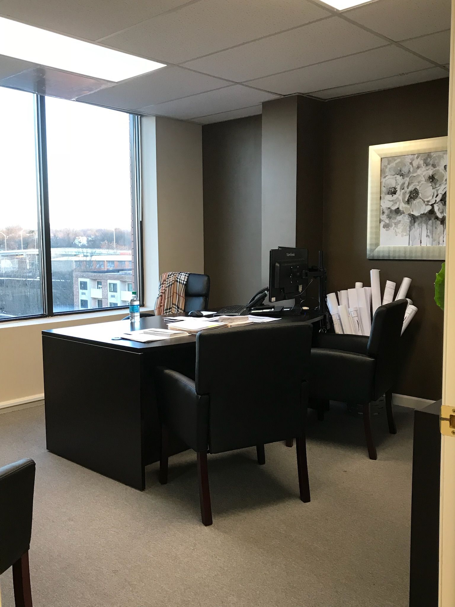 Office interior with desk, chairs, large window, and artwork on the wall.