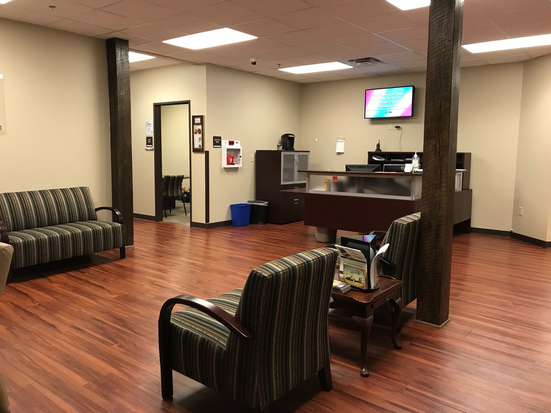 Waiting room with patterned chairs, wooden floor, and a reception desk.