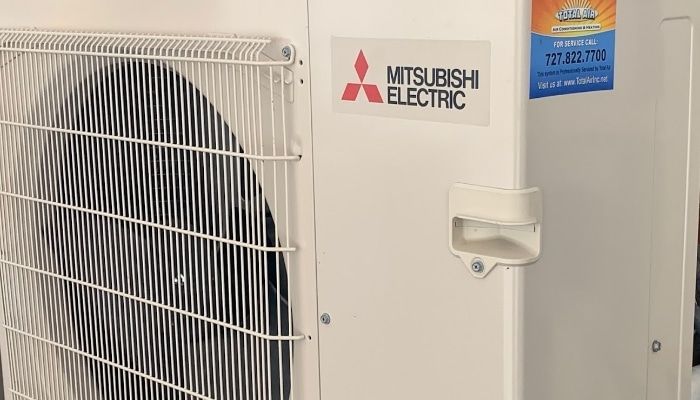 Mitsubishi Electric outdoor unit with fan and service sticker.
