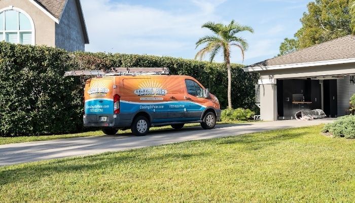 Solar panel installation van parked in a driveway in front of a house, palm tree in background.