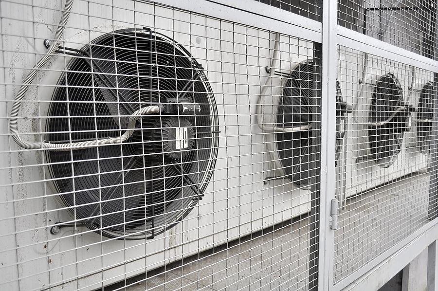 Three outdoor air conditioning units behind a protective wire mesh.
