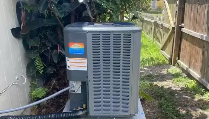 Air conditioning unit next to a white wall and a wooden fence.