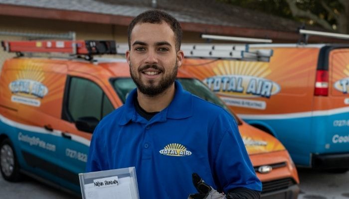 Man in blue shirt holding a clipboard in front of two Total Air vans.