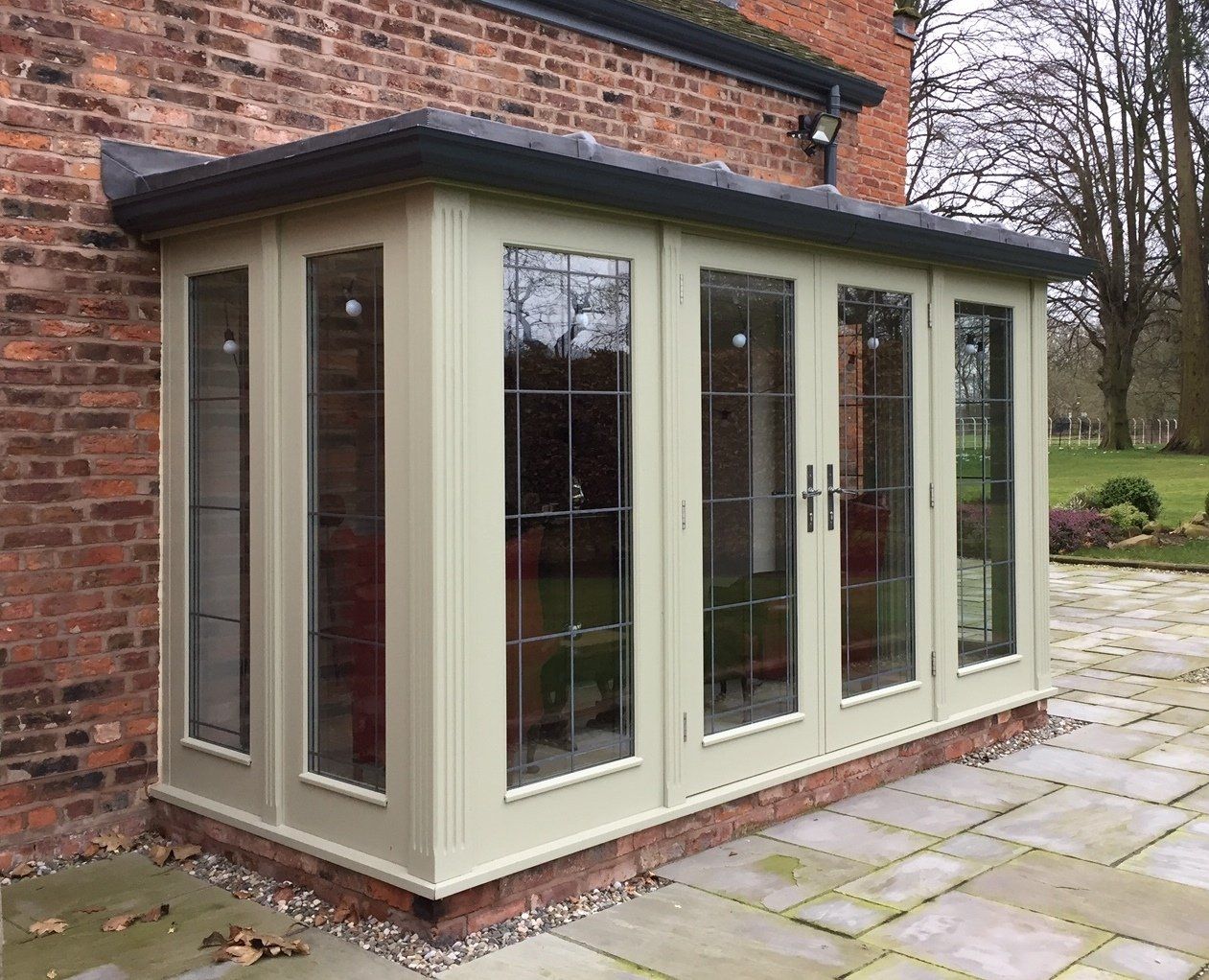 A light green sunroom with glass windows and doors attached to a brick building.