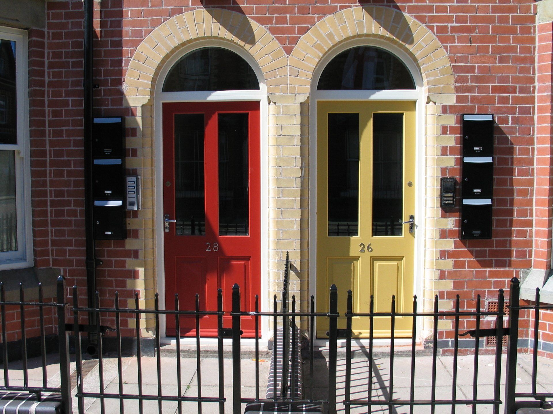 Red and yellow front doors on brick building, with arched entryways and black mailboxes.