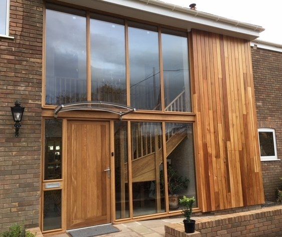 Modern home entryway with wooden door, glass windows, wood paneling, and a staircase.