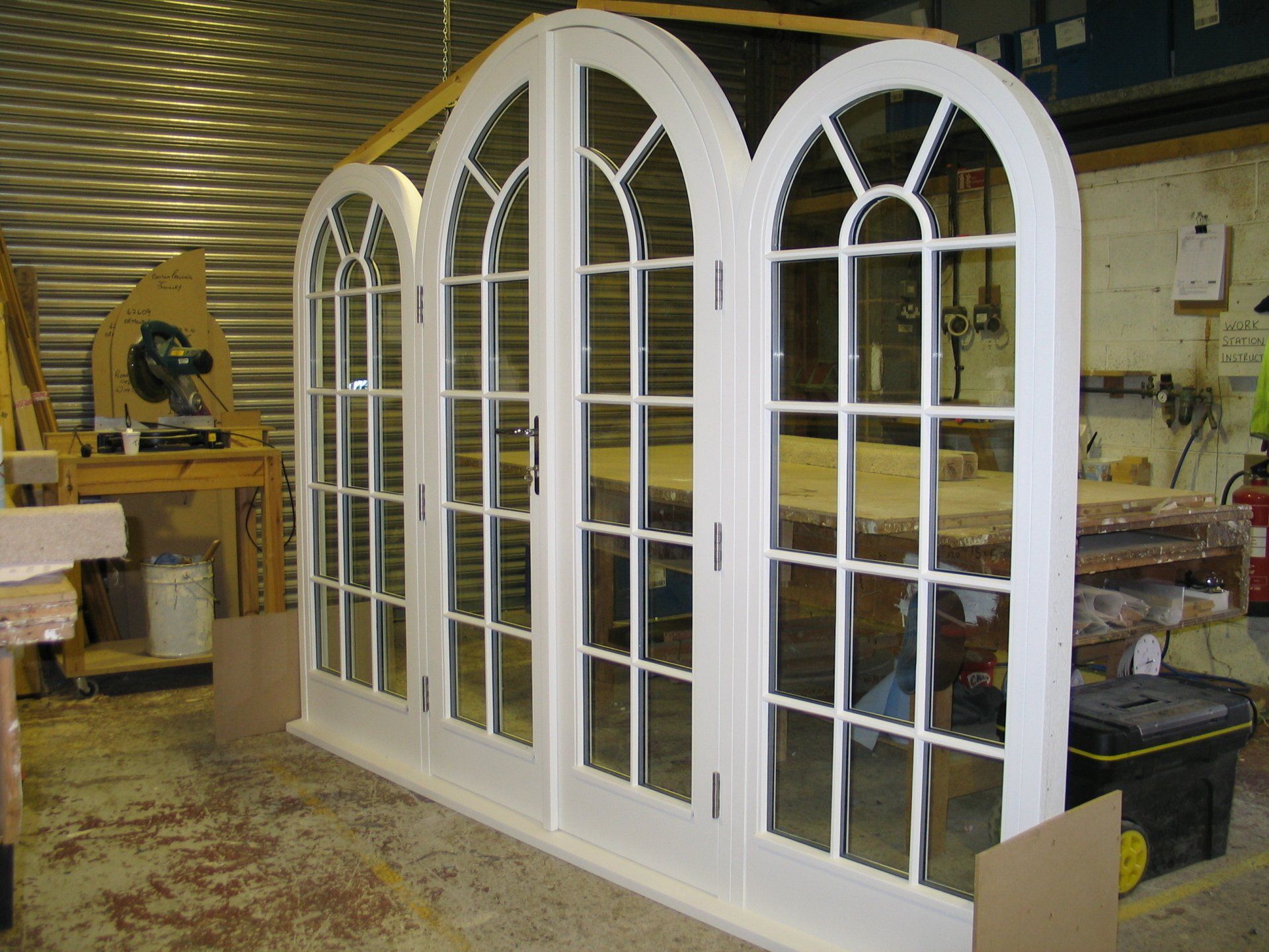 White-framed, arched-top French doors in a workshop setting, with glass panes and a dark handle.
