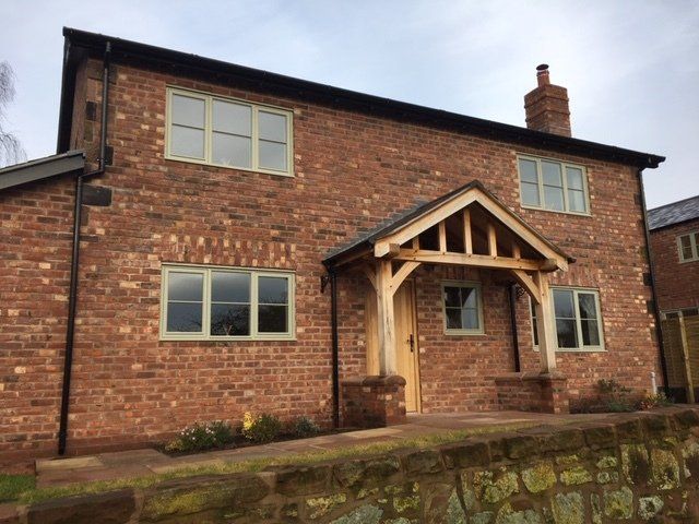 Red brick house with green-framed windows and a wooden porch; a cloudy sky.