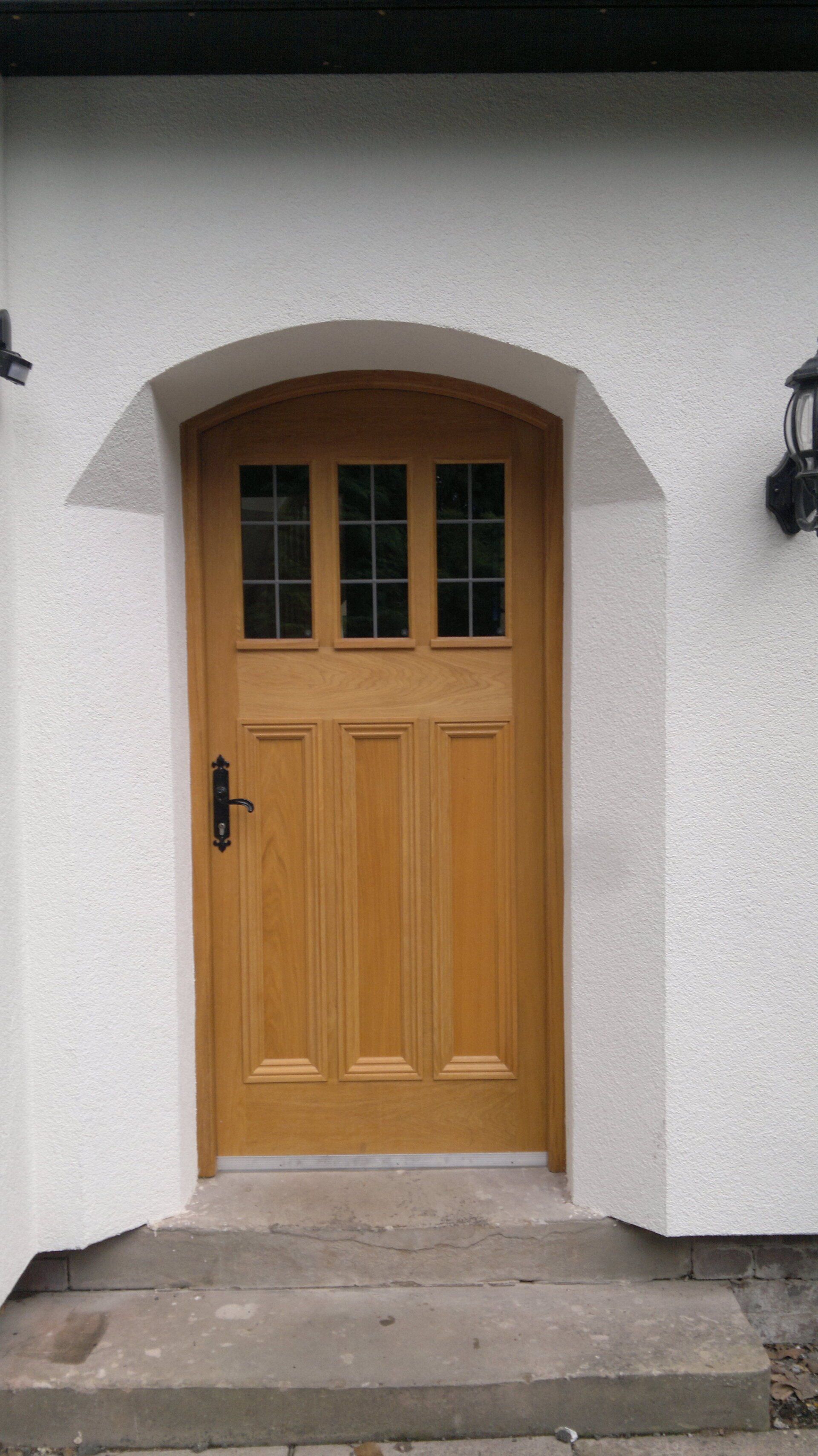 Wooden door with glass panes and arched white stucco surround.