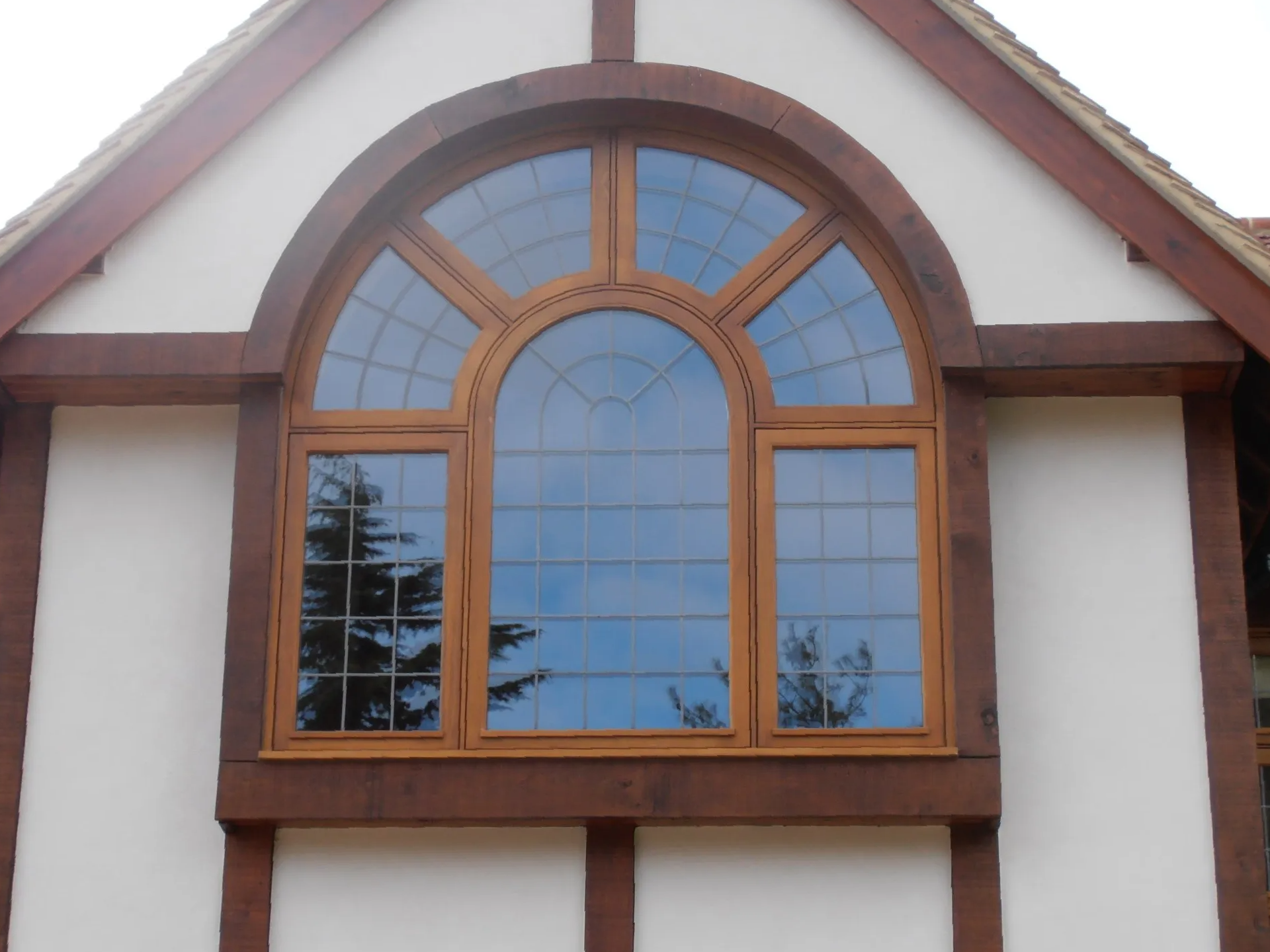 Large arched window with brown frame, set in a white wall with exposed brown beams.