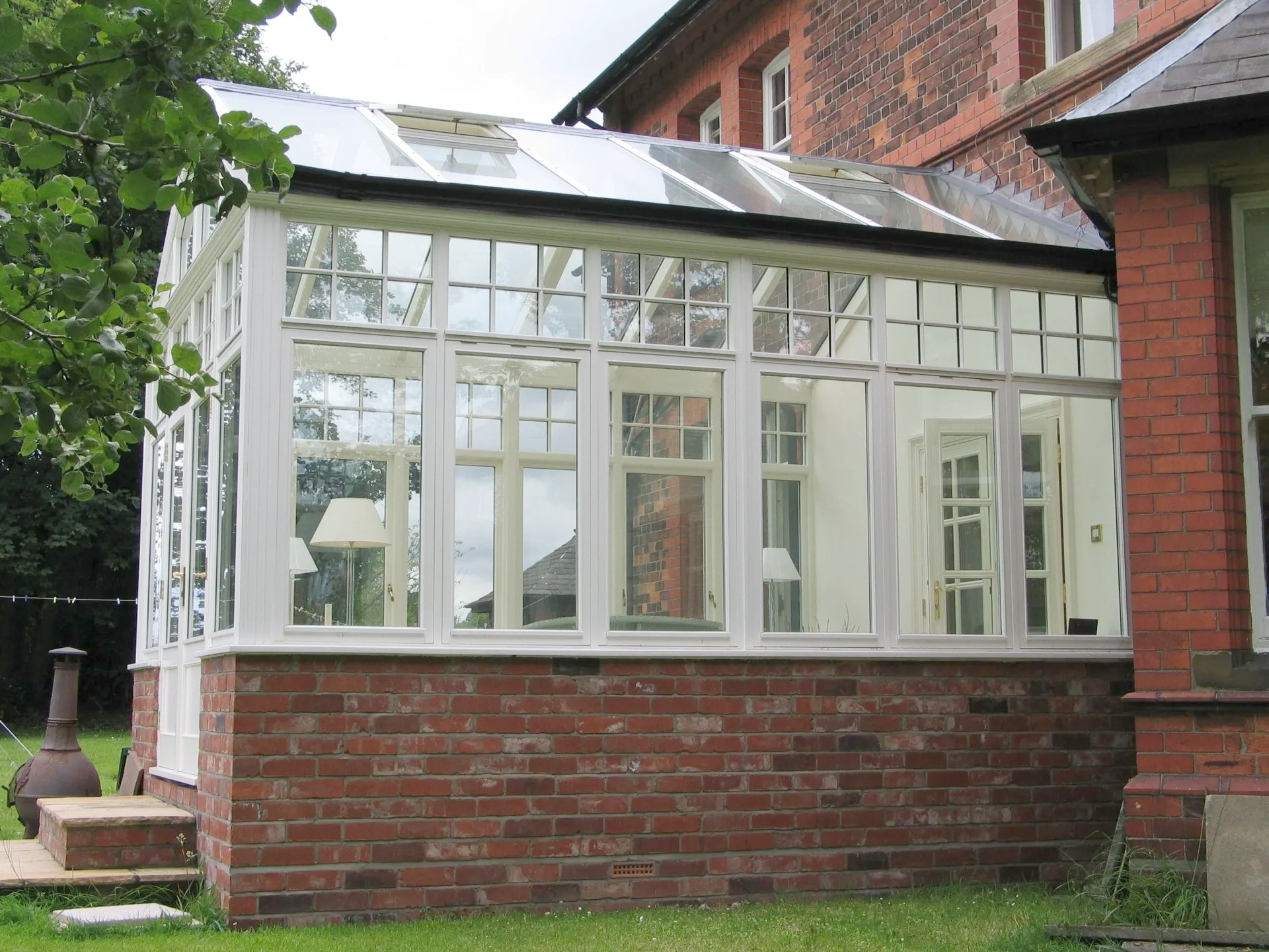 White-framed glass conservatory with red brick base attached to a brick building.