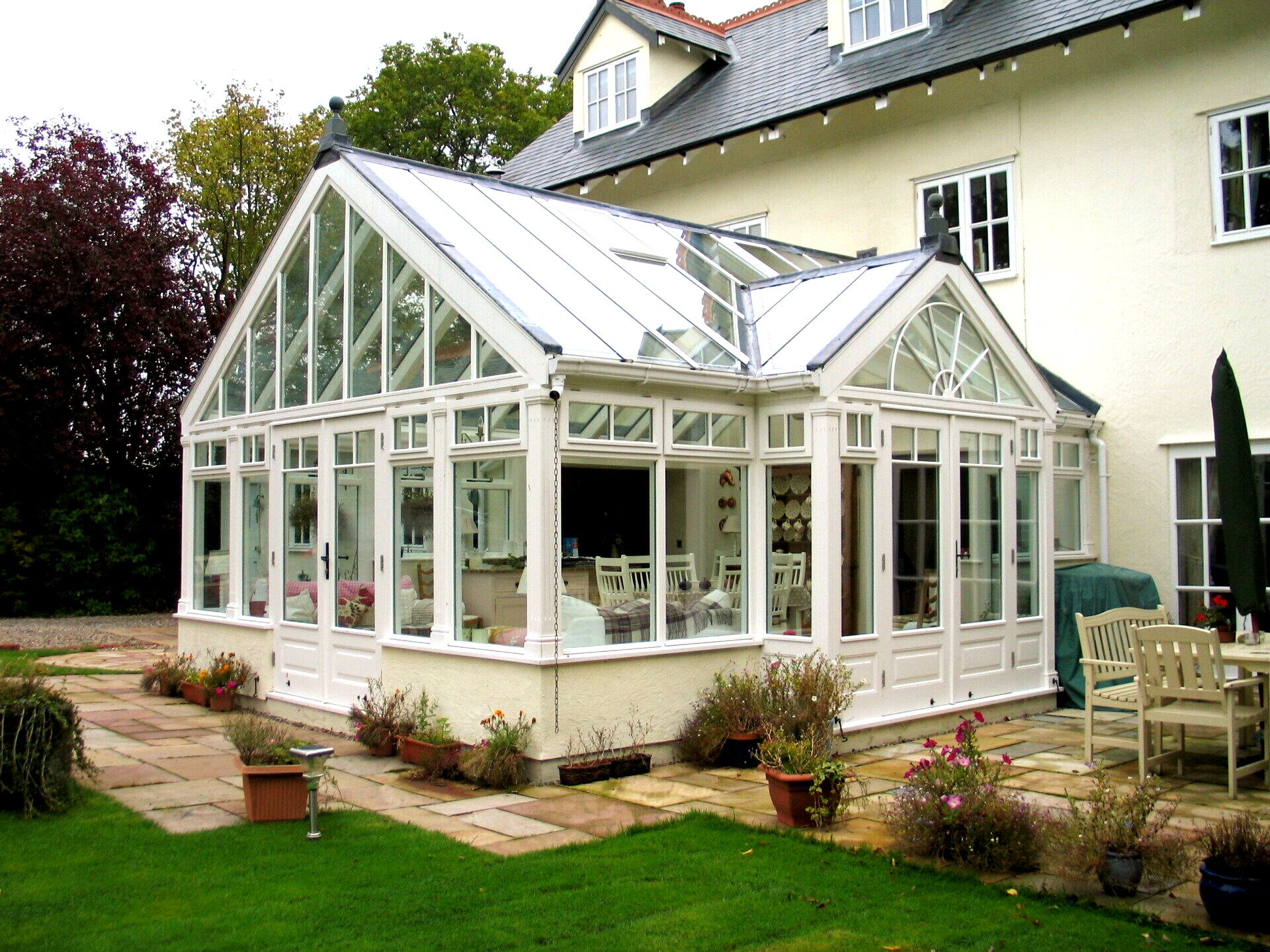 White conservatory attached to a white house; green lawn, patio, and potted plants in foreground.
