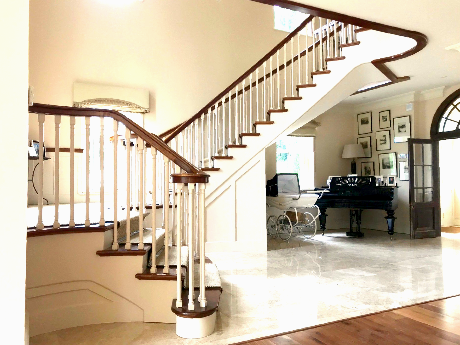 A grand staircase with white banisters and wooden steps in a bright, open foyer, leading to a room with a piano.
