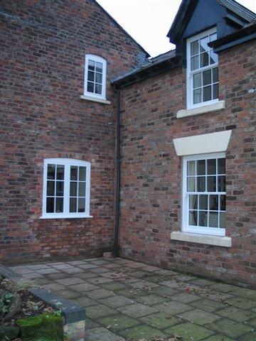 Brick building with white-framed windows; exterior view. Paved area in foreground, overcast sky.