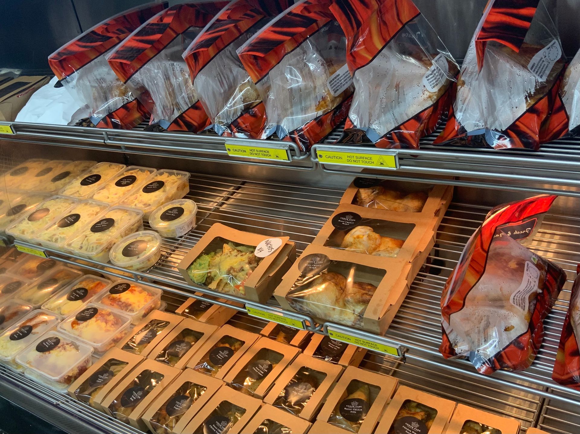 Hot roast chicken and prepared chicken meals on display in a deli cabinet — Cedar Park Supermarket In Taranganba, QLD