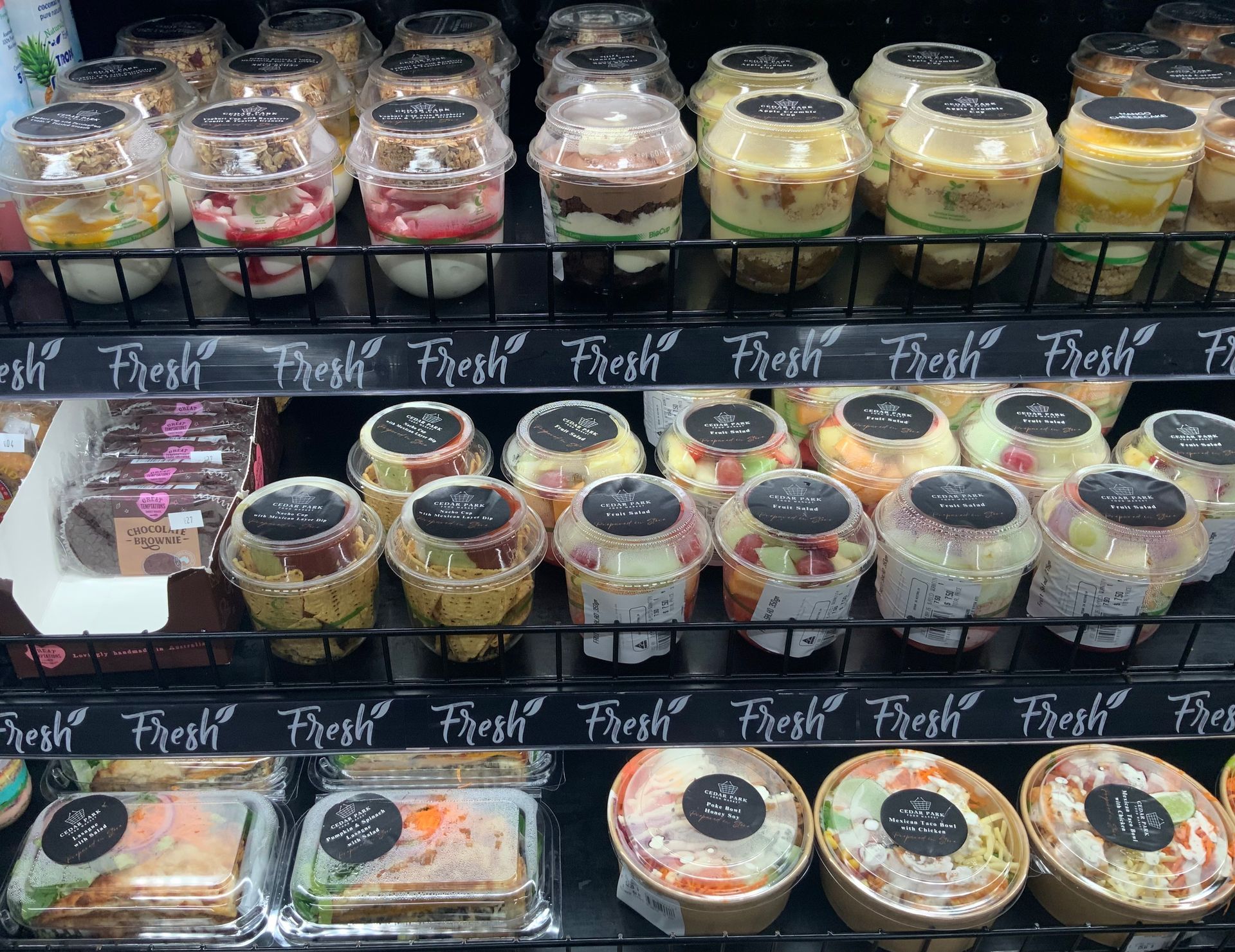 Display case of assorted packaged fruit desserts in cups and slices on black shelves