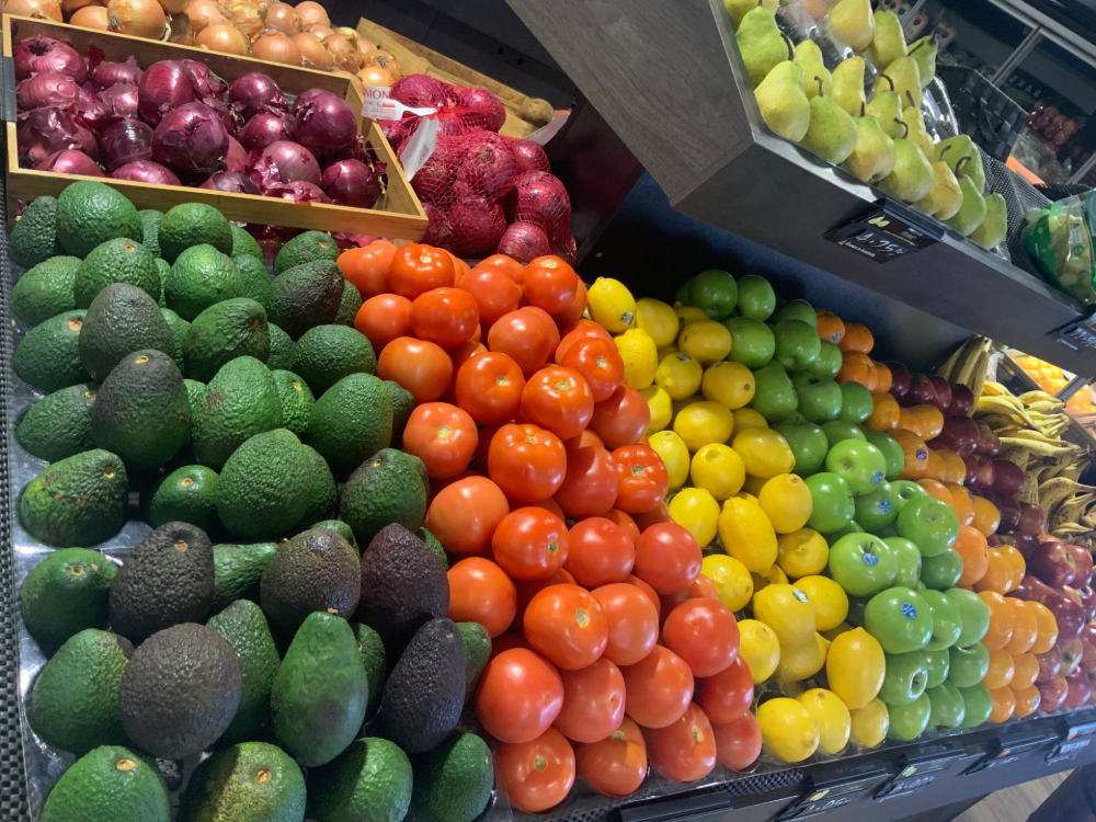 Colorful stacks of avocados, oranges, lemons, limes, and plums at a grocery produce display