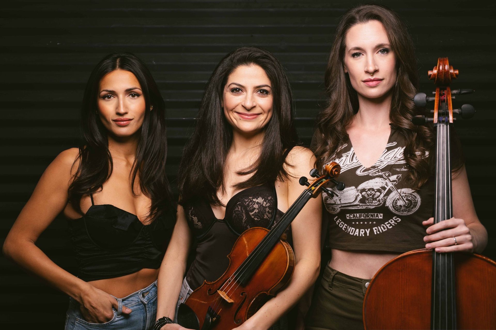 Three women are standing next to each other holding violins and cello.