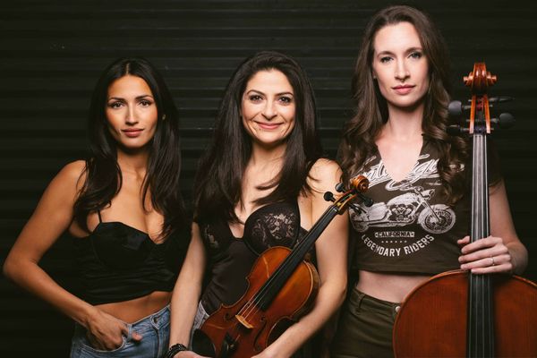 Three women are standing next to each other holding violins and cello.