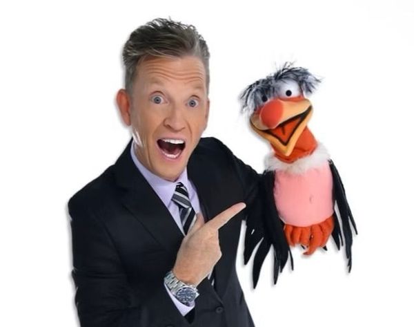 A man in a suit is pointing at a bird puppet