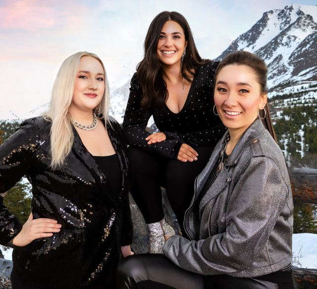 Three women are posing for a picture with a mountain in the background