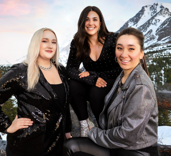 Three women are posing for a picture with a mountain in the background