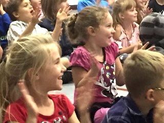 A group of children are sitting in a classroom clapping their hands.