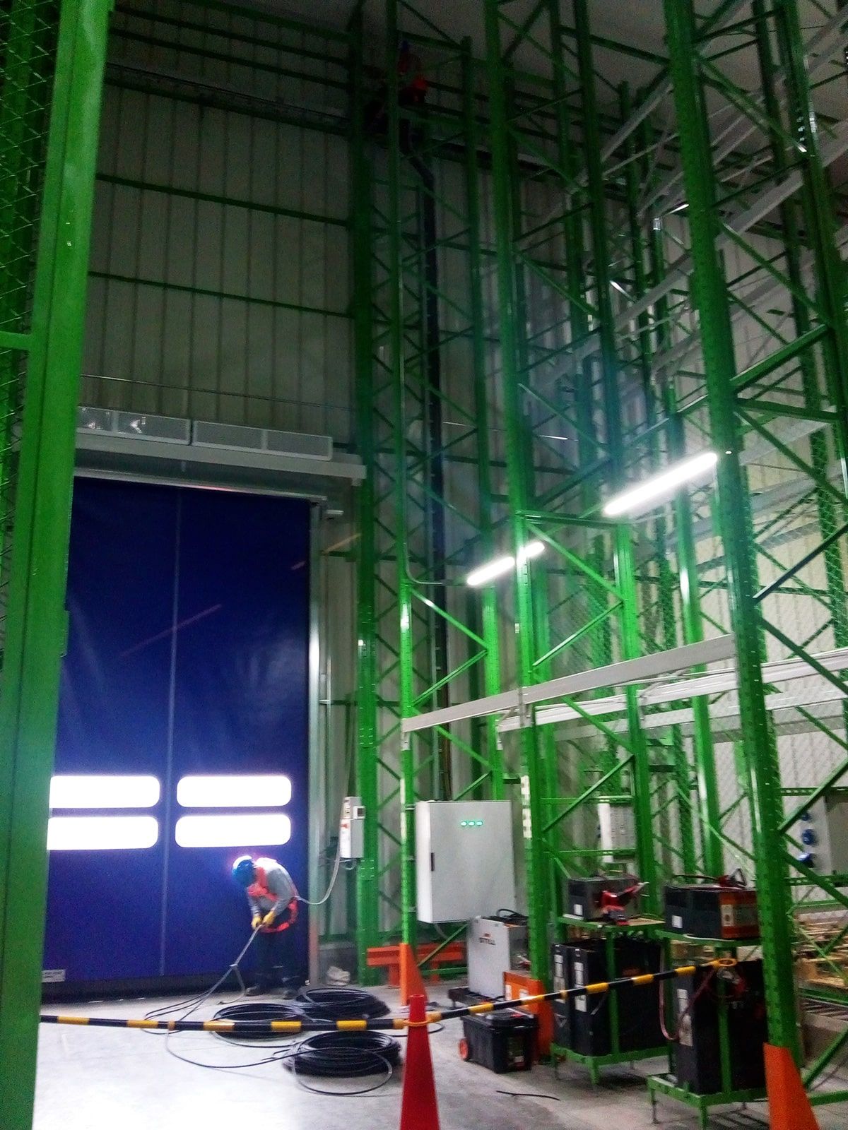 Un hombre está trabajando en un almacén con estantes verdes y una puerta azul.