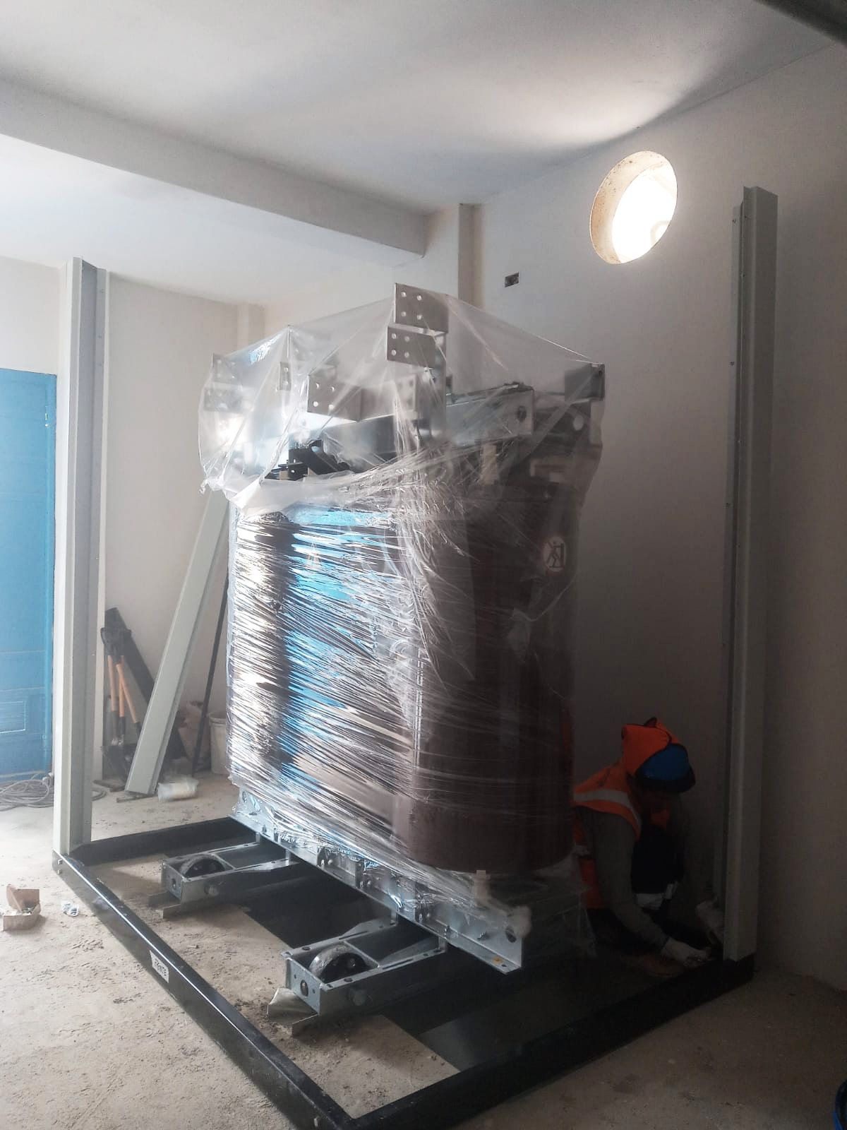 Un gran transformador está envuelto en plástico y colocado sobre un marco de metal en una habitación.