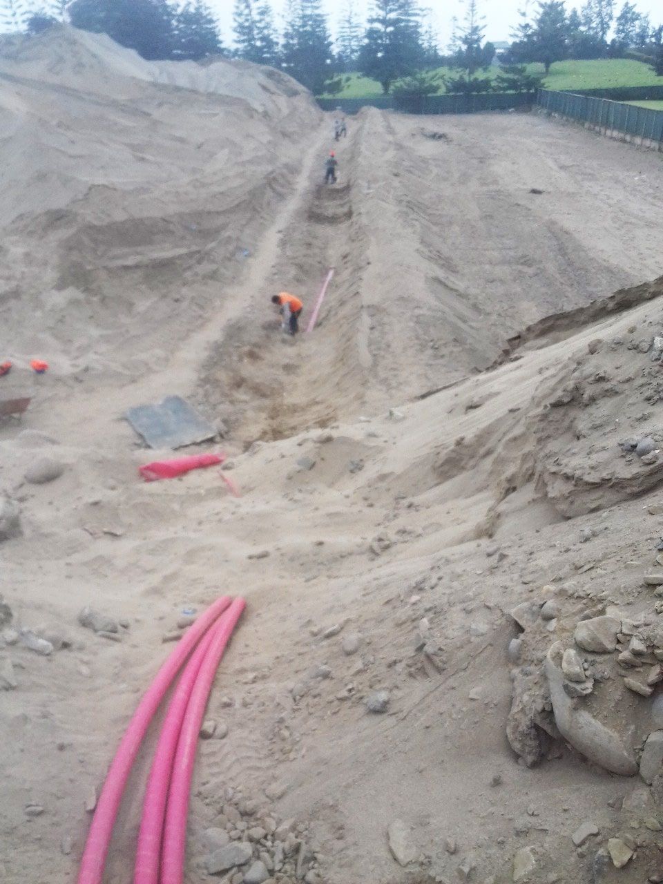 Un hombre está cavando en la tierra con una pipa rosa en primer plano.