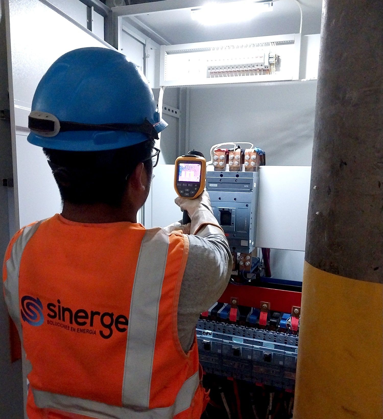 Un hombre que llevaba un casco azul y un chaleco naranja con la palabra sinergi en la espalda.