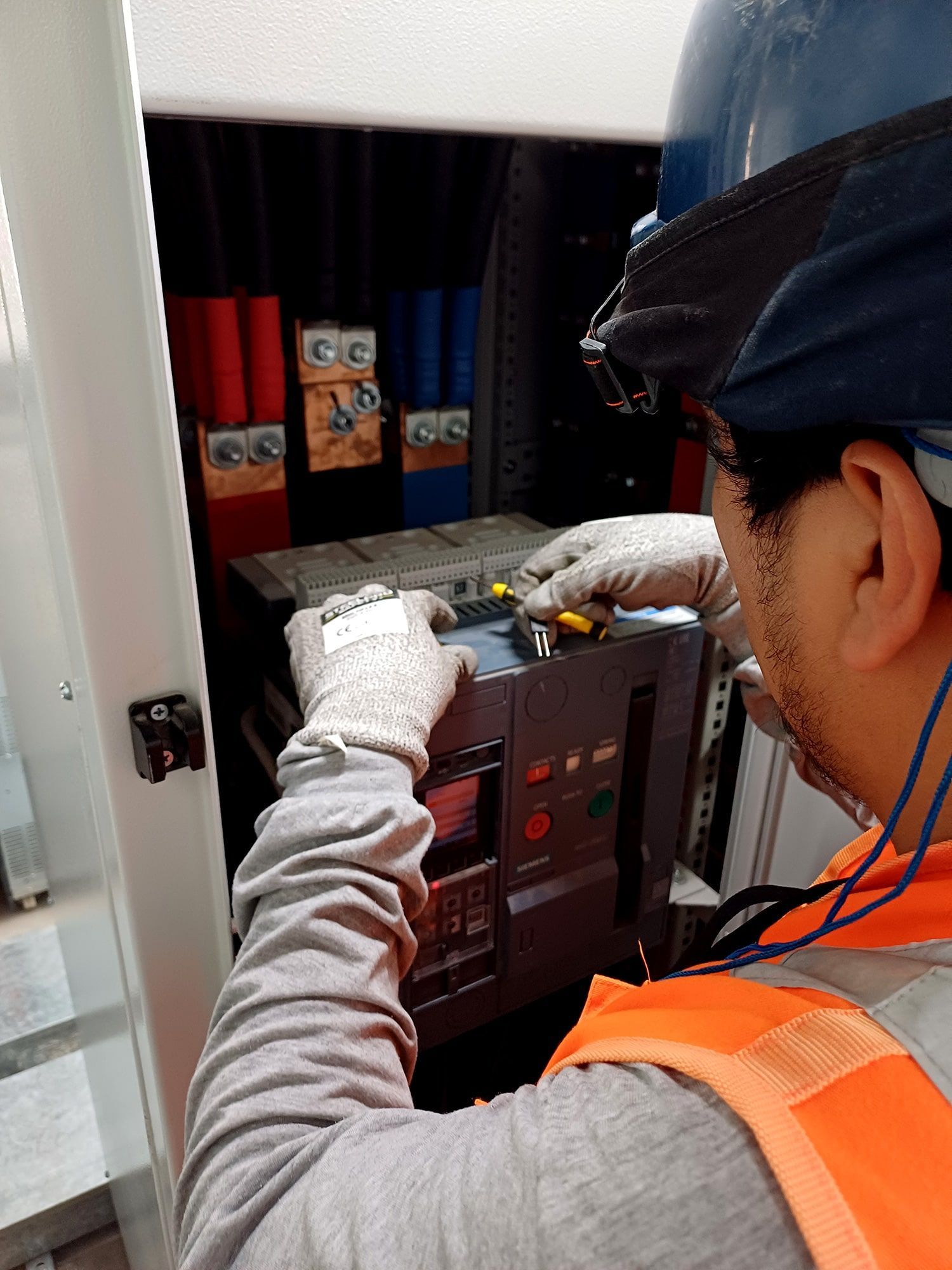 Un hombre con casco y chaleco naranja está trabajando en una caja eléctrica.