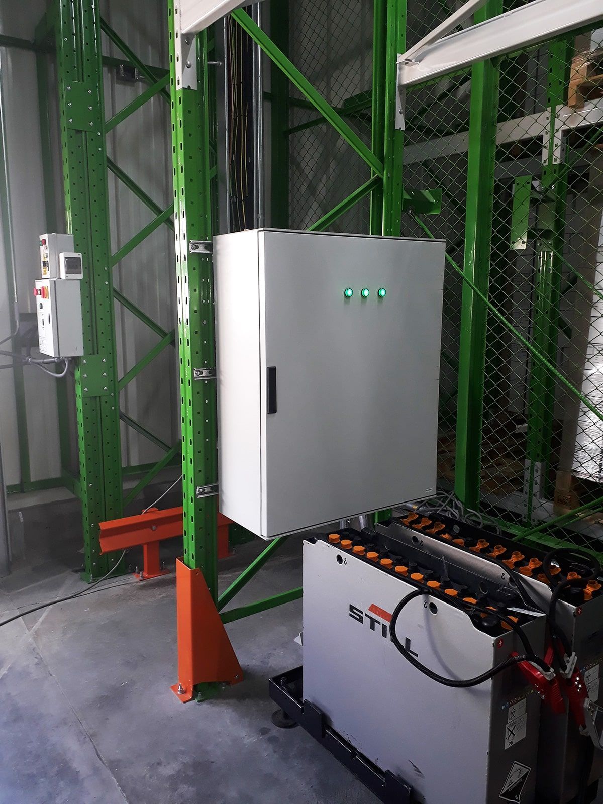 Un almacén con estantes verdes y una caja blanca en la pared.