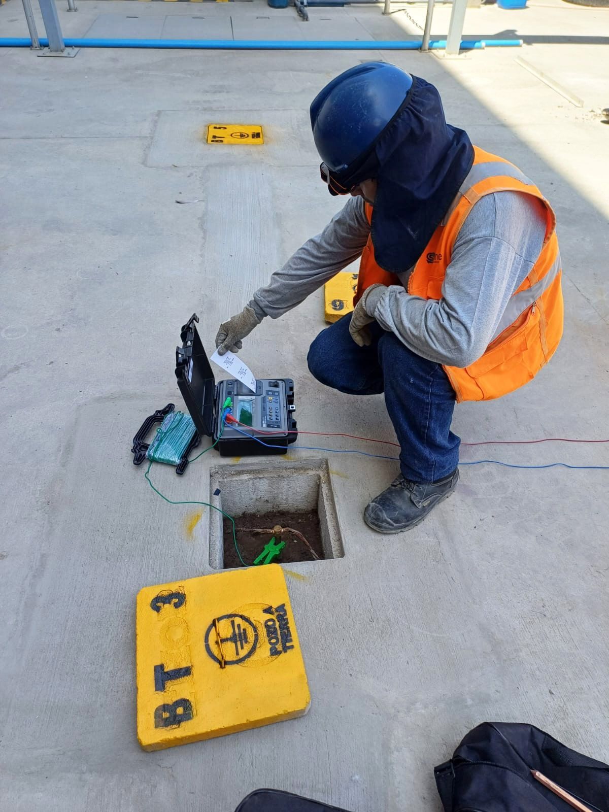 Un hombre con un chaleco naranja está arrodillado en un agujero en el suelo.