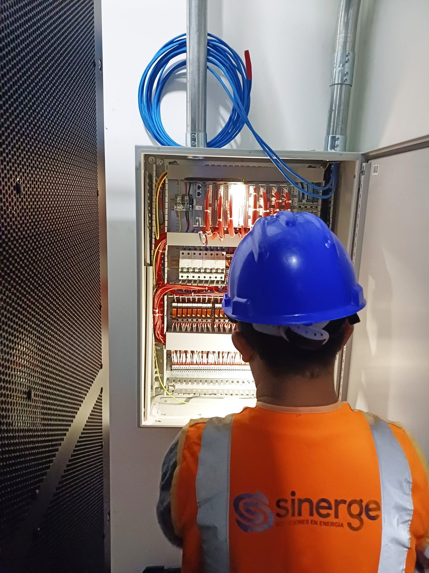 Un hombre que lleva un casco azul está trabajando en una caja eléctrica.