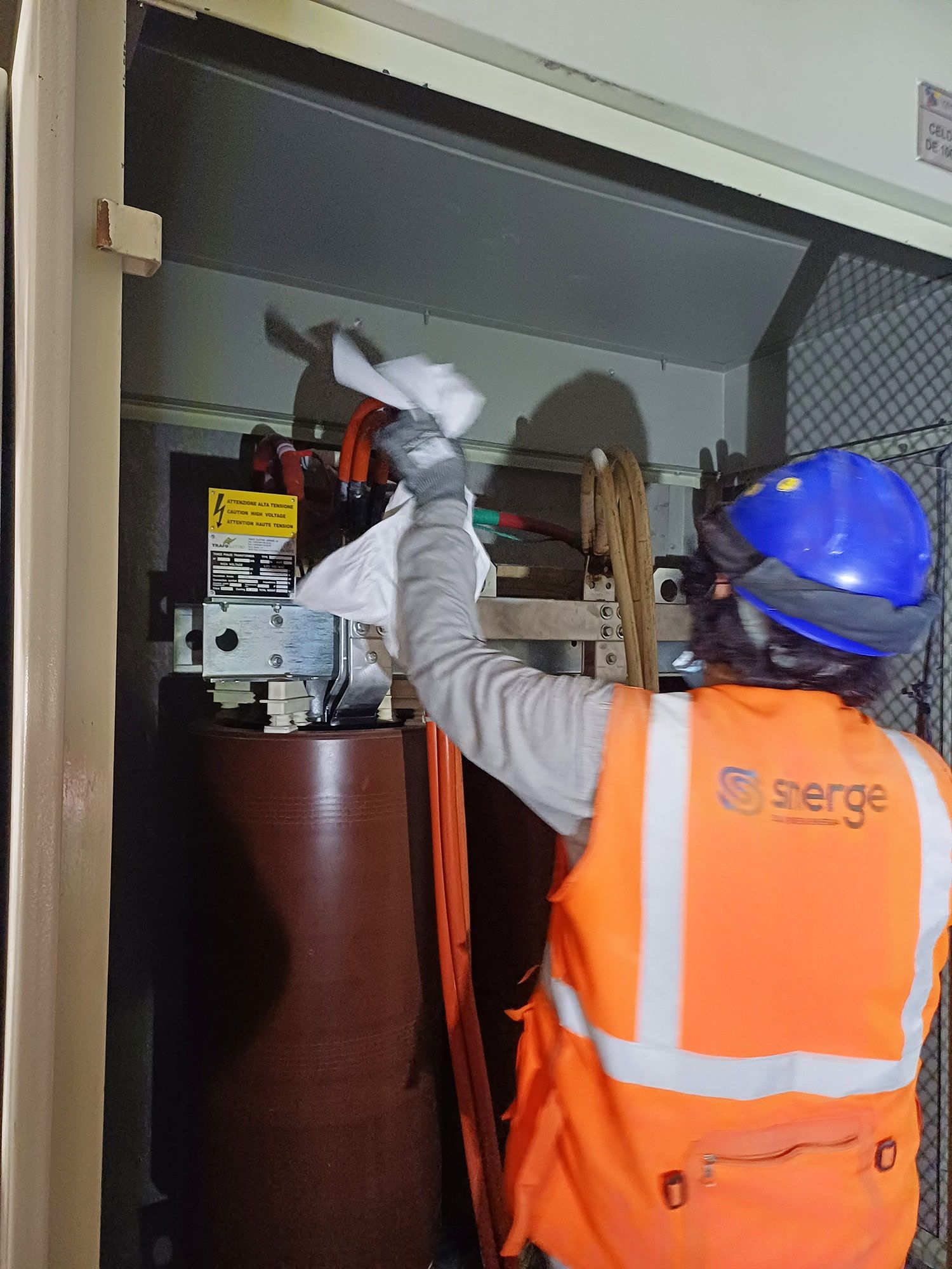 Un hombre con un chaleco naranja y un casco azul está limpiando una máquina.