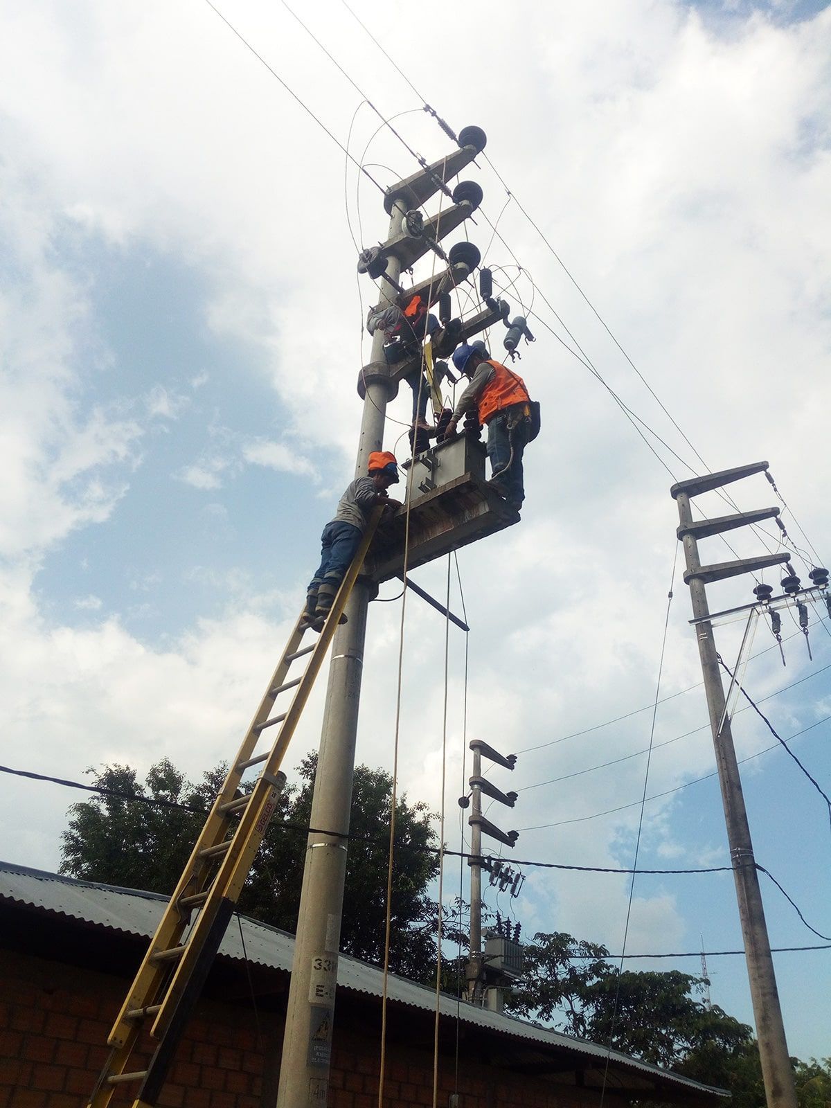 Dos hombres están trabajando en un poste de electricidad con una escalera.