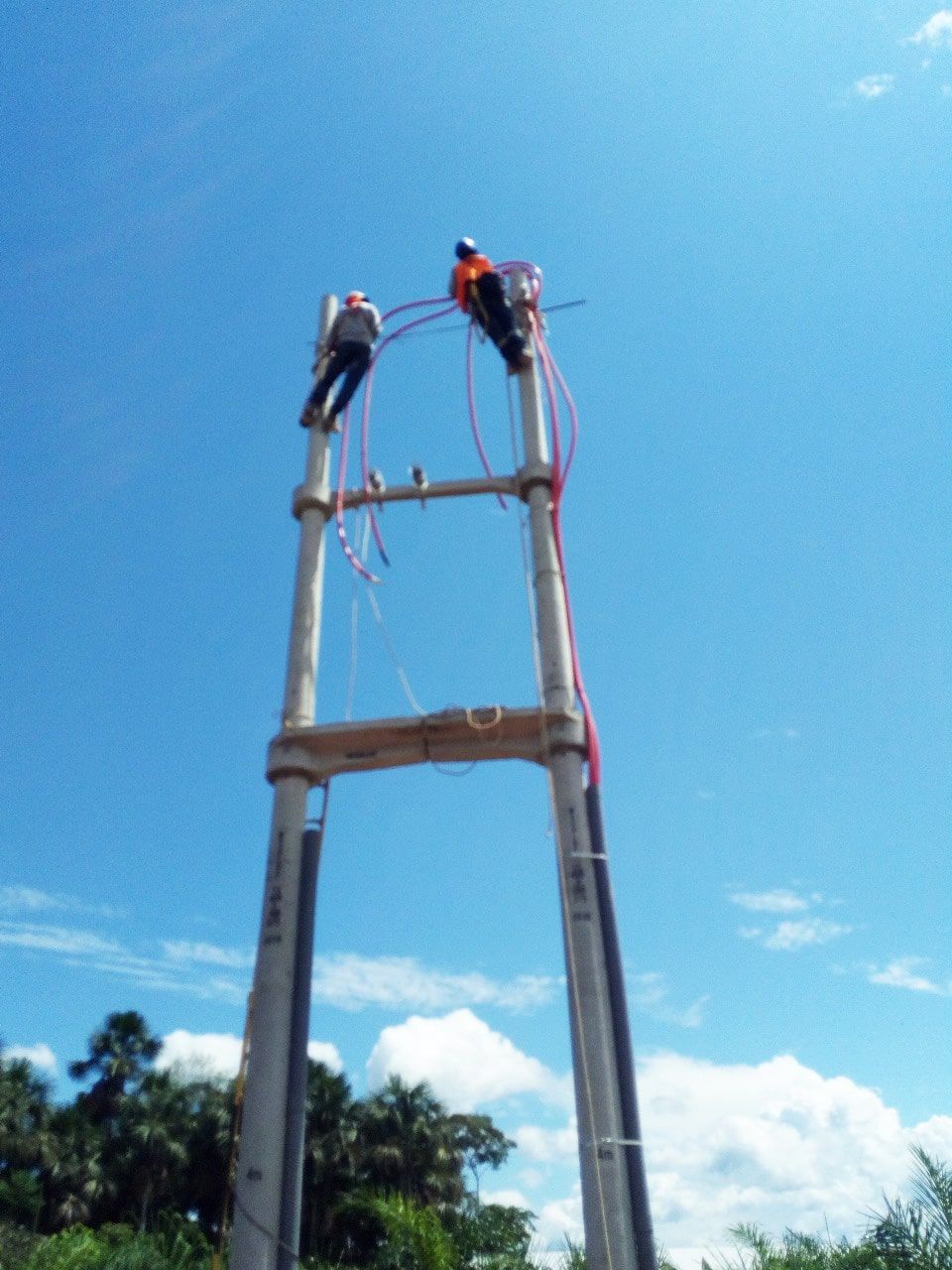 Dos hombres están trabajando en un poste muy alto.